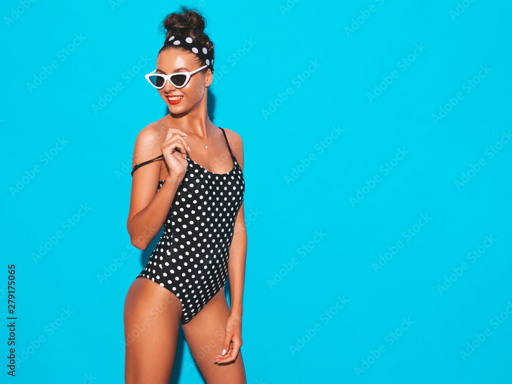 Young beautiful sexy smiling hipster woman in sunglasses.Trendy girl in summer peas swimwear bathing suit. Positive female going crazy.Funny model isolated on blue