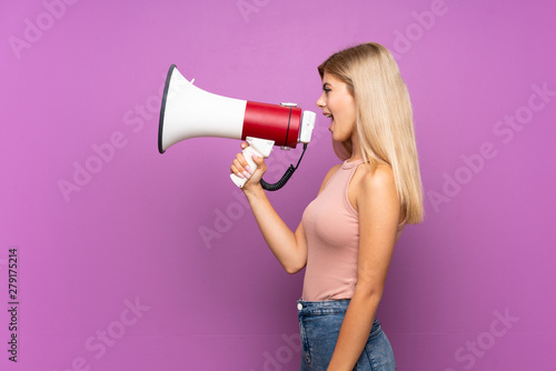 Teenager girl over isolated purple background shouting through a megaphone