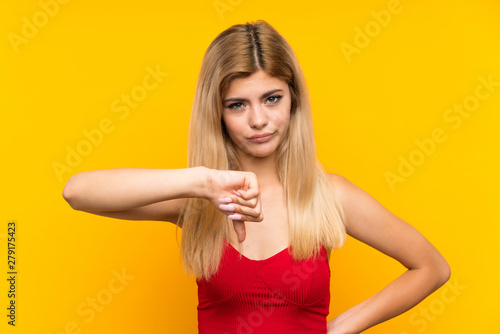 Teenager girl over isolated yellow background showing thumb down sign