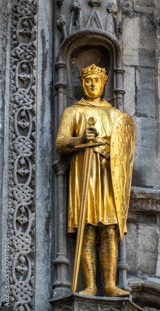 Bruges, Flanders, Belgium -  June 17, 2019: Detail with golden Noblity statue of facade of Basilica of the Holy Blood on the Burg square. Set in dark gray stone facade with stained windows.