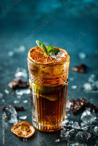 Fresh cocktail with cola, lime, chocolate and ice in glass on dark blue background. Summer cold drink and cocktail, selective focus