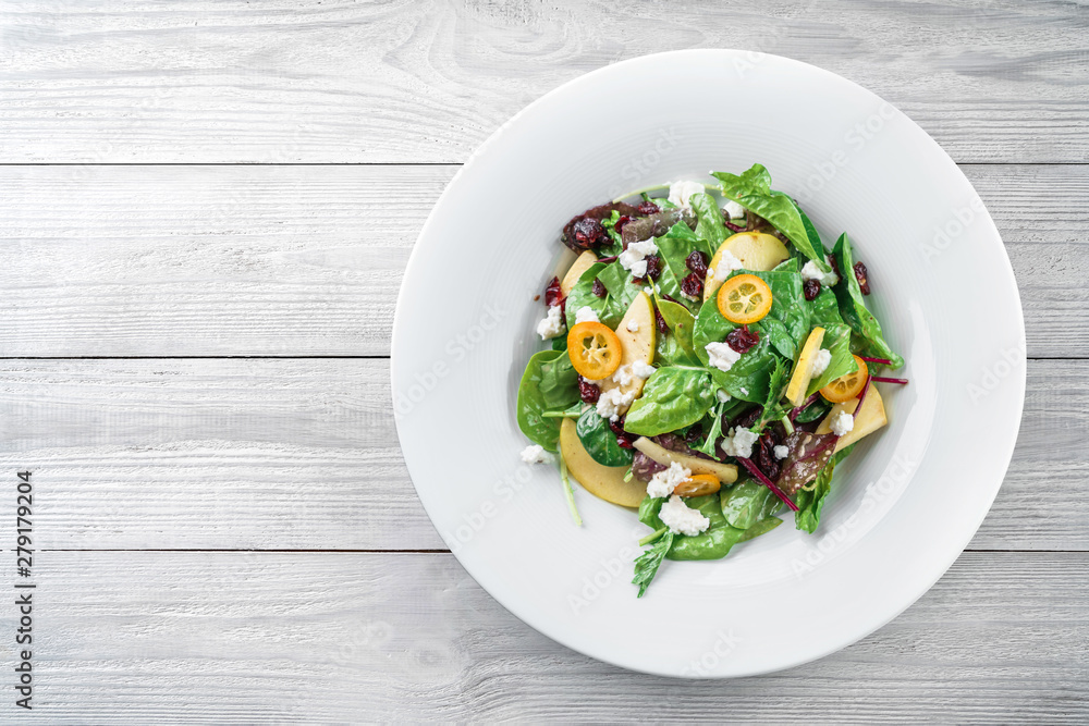 Healthy fresh salad with mix greens, apple, cream cheese, cranberry, sauce and edible flowers in plate on light wooden background. Healthy food, vegetarian dieting, top view Healthy fresh salad with mix greens, apple, cream cheese, cranberry, sauce and edible flowers in plate on light wooden background. Healthy food, vegetarian dieting, top view