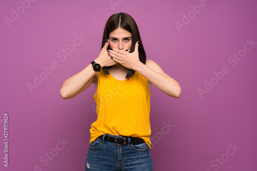 Young woman over isolated purple wall covering mouth with hands