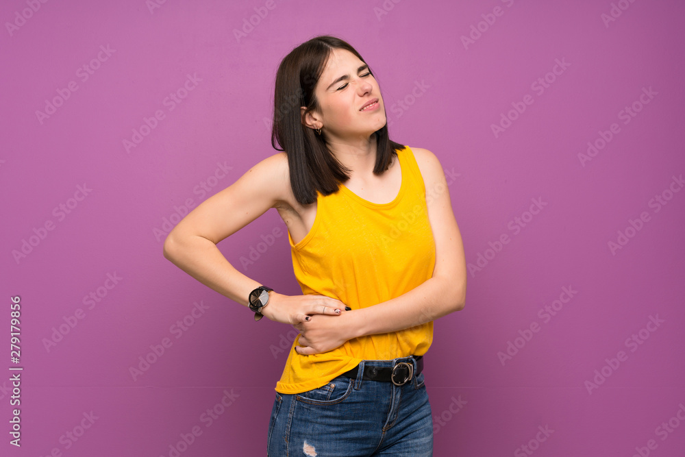 Young woman over isolated purple wall suffering from backache for having made an effort Young woman over isolated purple wall suffering from backache for having made an effort