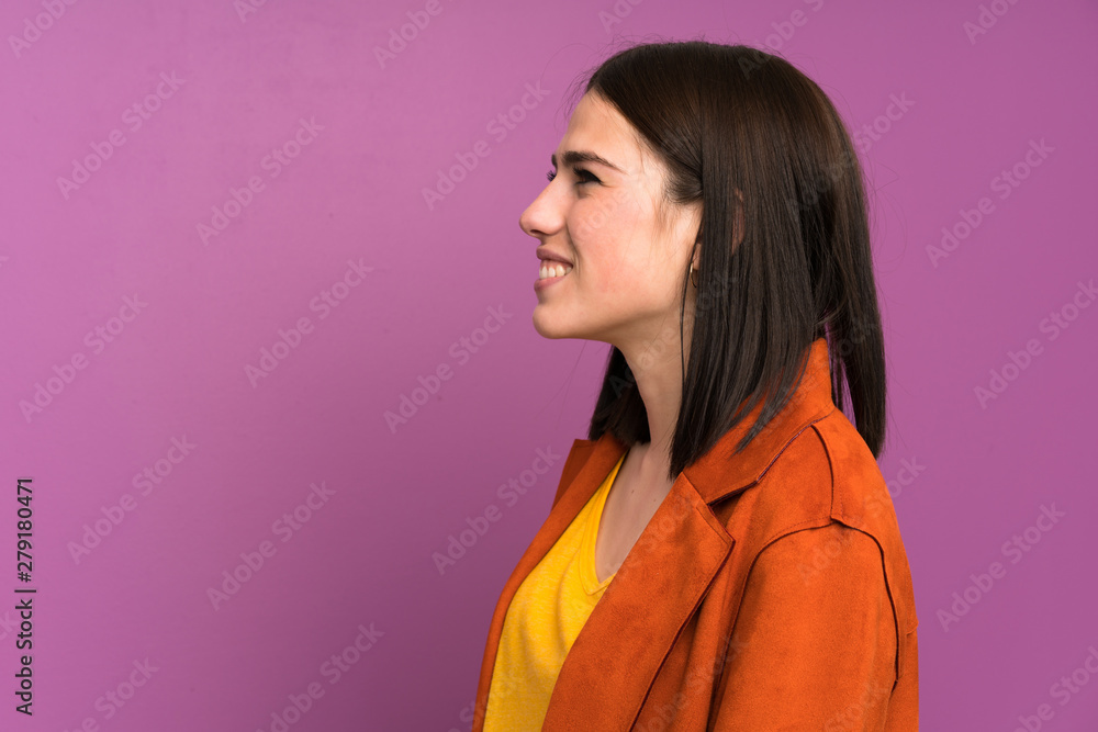 Young woman with a coat over isolated purple background standing and looking to the side Young woman with a coat over isolated purple background standing and looking to the side