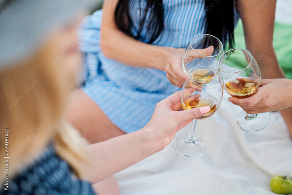Three female hands with glasses of white wine. Toast, congratulations on an outdoor picnic. The concept of relaxation and companionship.