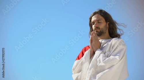 Man in robe praying to God against blue sky background, asking soul salvation photo