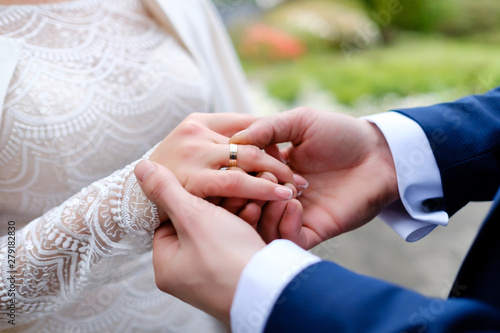 wedding details - Groom wears bride wedding gold ring at ceremony outdoor in spring time