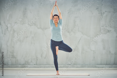 Full length of beautiful Caucasian brunette doing Tree yoga pose on mat barefoot. photo