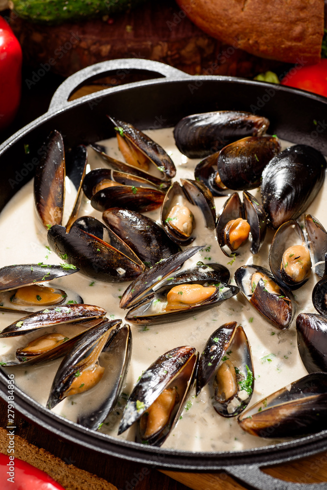 Mussel shells in cream sauce in a black cauldron on a dark wooden background, decorated with vegetables Mussel shells in cream sauce in a black cauldron on a dark wooden background, decorated with vegetables