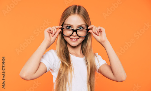 Close up portrait of happy, funny and beautiful blonde little girl in glasses is posing over yellow background. Study, education, school, university, college, graduate concept.