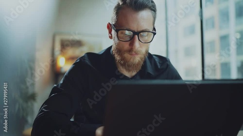 Bearded businessman man working at sunny office on desktop computer while sitting at wooden table.