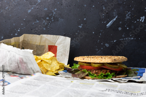 Delicious, healthy vegan burger placed on old vintage newspaper with chips on a black distressed background photo