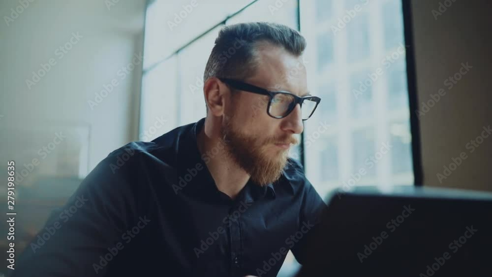 Bearded businessman man working at sunny office on desktop computer while sitting at wooden table. Bearded businessman man working at sunny office on desktop computer while sitting at wooden table.