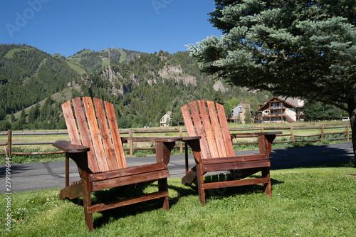 Two empty wood adirondack chairs sit on grass, overlooking the Sawtooth mountains of Idaho. Taken in Ketchum, ID photo
