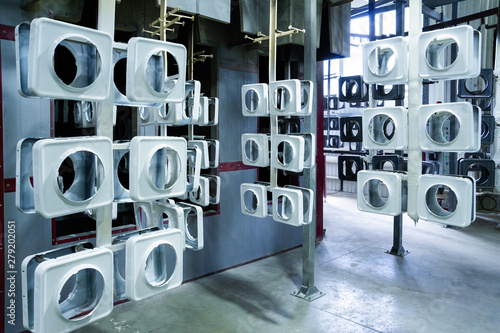 line for painting metal products in white color coating. Square metal products with a round hole hang on mounts after powder painting