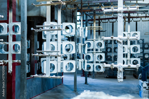 line for painting metal products in white color coating. Square metal products with a round hole hang on mounts after powder painting