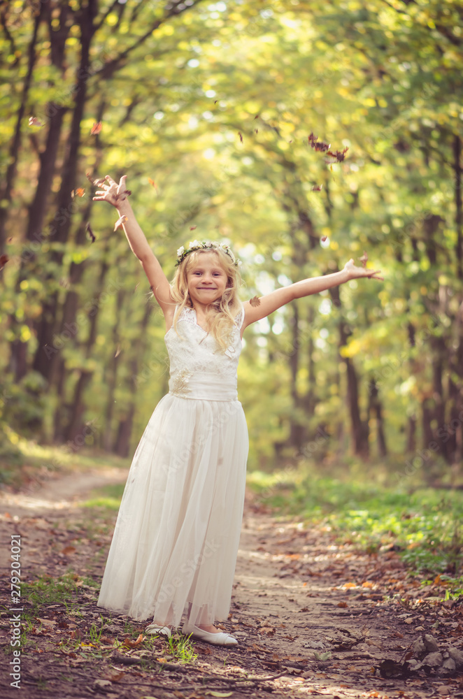 adorable blond girl with leaves in hands in sunny day in magical forest