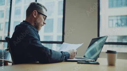 Bearded businessman man working at sunny office on desktop computer while sitting at wooden table.