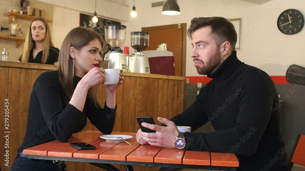 Close-up of happy cheerful teenagers sitting in a cafe at a table looking at the phone screen and laughing pointing a finger at the screen. Slow motion. Couple in coffee shop connected with smartphone Close-up of happy cheerful teenagers sitting in a cafe at a table looking at the phone screen and laughing pointing a finger at the screen. Slow motion. Couple in coffee shop connected with smartphone