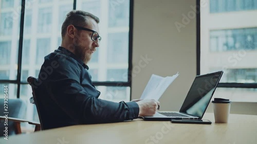 Bearded businessman man working at sunny office on desktop computer while sitting at wooden table.