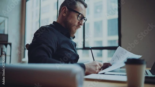 Bearded businessman man working at sunny office on desktop computer while sitting at wooden table.