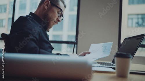 Bearded businessman man working at sunny office on desktop computer while sitting at wooden table.
