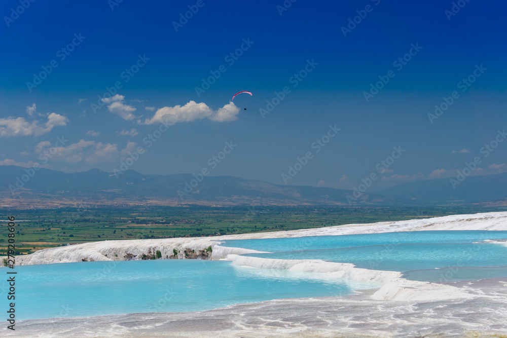 Blue travertine pools and terraces in Pamukkale, Denizli, Turkey. Cotton castle. Paragliding in the sky.