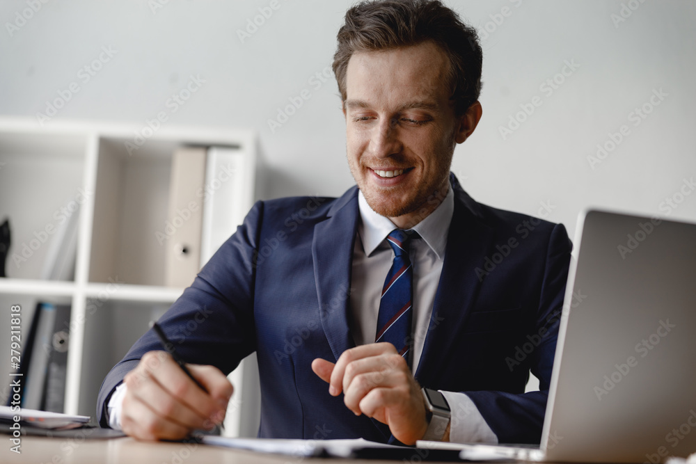Positive man smiling while signing the documents Positive man smiling while signing the documents