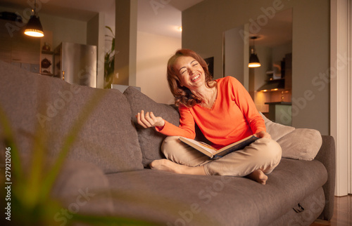 one woman laughing, while relaxing in her sofa, at home. looking at camera.