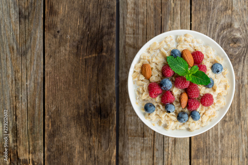 Oatmeal with raspberries, almonds and blueberries and mint on old wood background