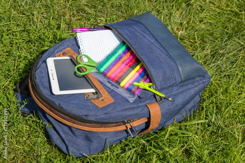 school backpack,blue backpack with school accessories of lying on the grass photo