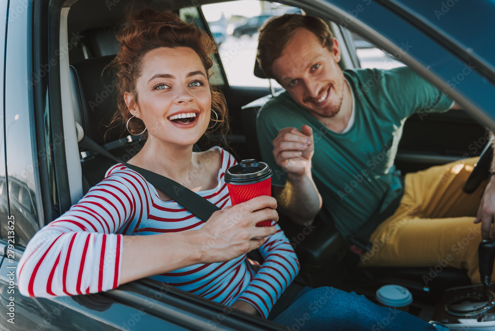Charming young woman with hot drink and her friend sitting in the car