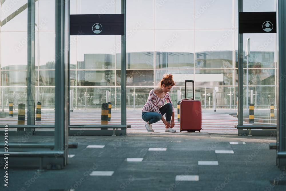 Young woman with travel luggage bag tying her sneakers in airport Young woman with travel luggage bag tying her sneakers in airport