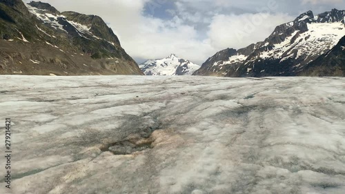 Aerial, low, drone shot, close to the ice fields surface, at Aletsch Glacier, snowy Bernese alpine, mountain peaks, in the background, on a partly sunny day, in Jungfrau region, Wallis, Switzerland photo