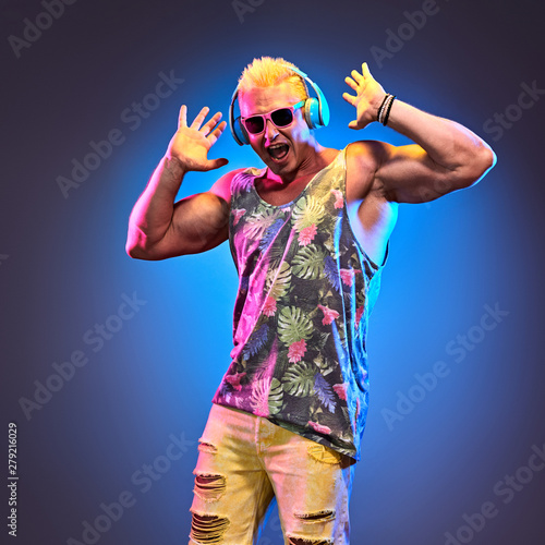 Fashion Excited Muscular DJ man dance music, colorful neon light. Handsome pumped-up blonde expressive guy happy relax. Art neon fashionable style. Mixing dj music lover nightclub,summer party concept
