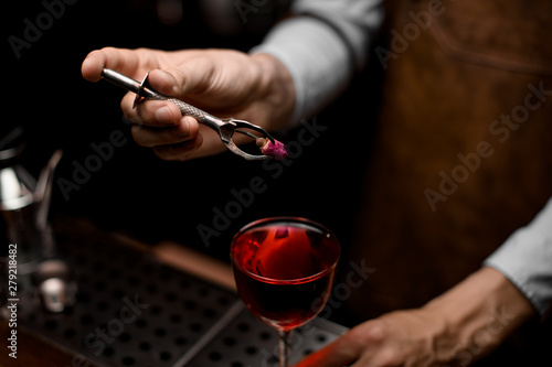 Bartender putting a little rose bud to the red cocktail in the glass