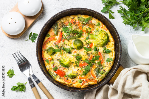 Frittata with vegetables on white stone table.