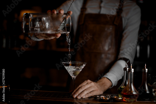 Bartender pouring a transparent alcoholic drink from the measuring cup to the martini glass