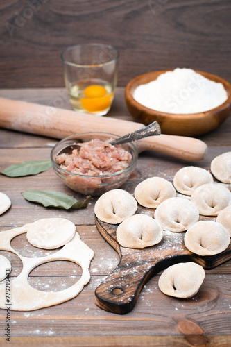 Raw dumplings on the cutting board and ingredients for their preparation: flour, egg, minced meat on a wooden table