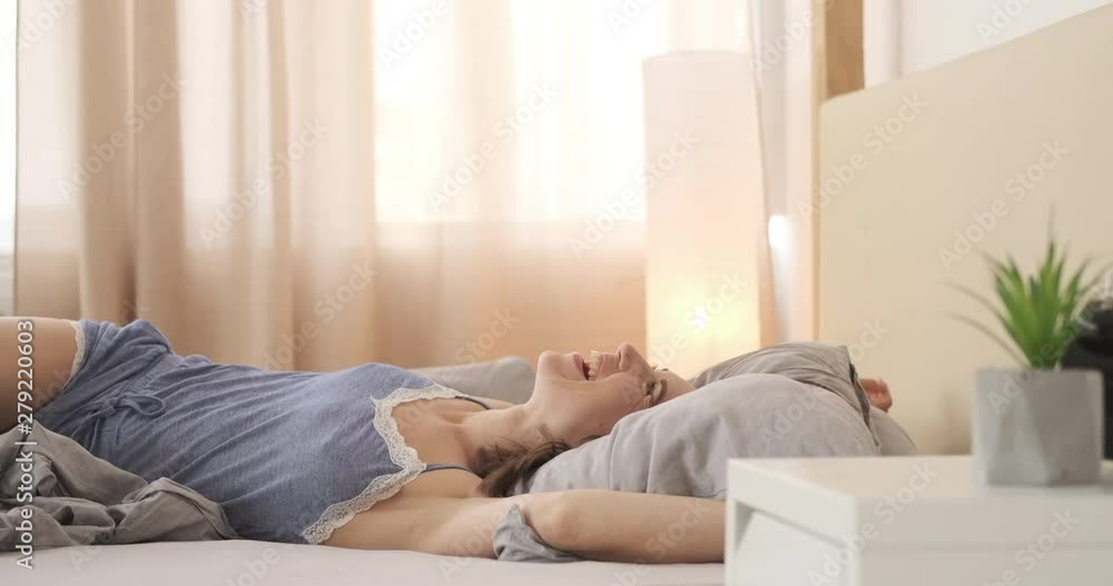 Happy young woman in nightdress falling backward on her bed Happy young woman in nightdress falling backward on her bed
