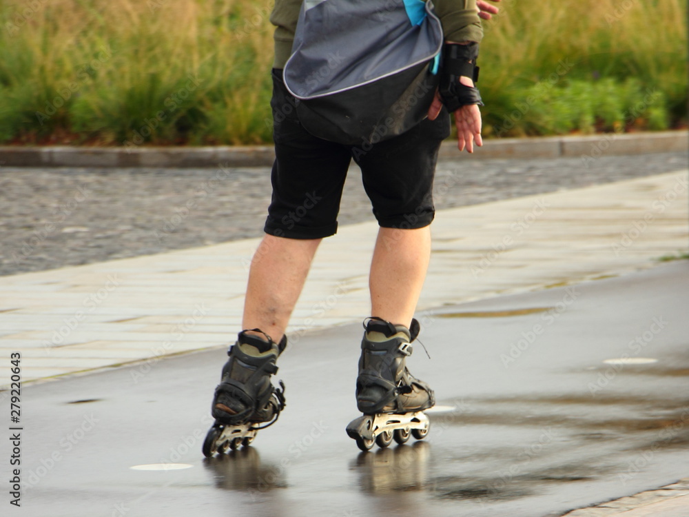 An elderly man rides on roller blades on a wet bike path in the Park on a summer day after rain, feet close-up, ecological city transport