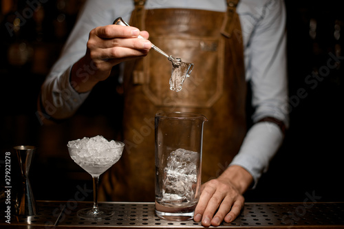 Male bartender putting an ice cube to the measuring glass cup
