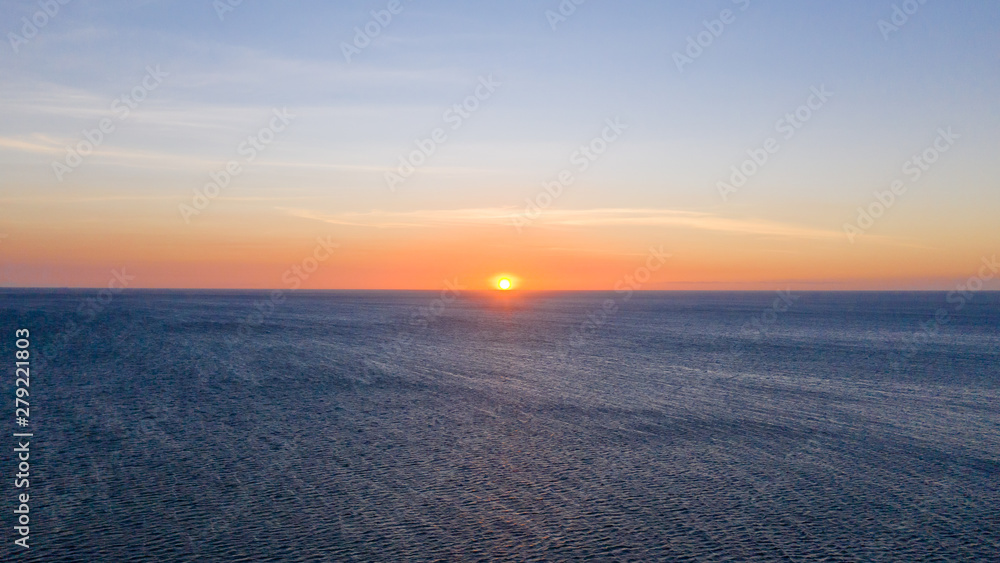 Sunset over the sea in clear weather, view from above. Seascape with evening sun and deep blue sea.