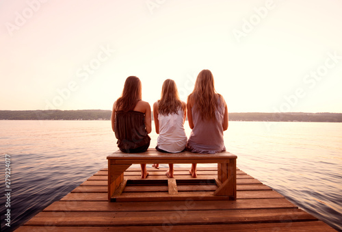 Rear view of three women sitting on pier at lake