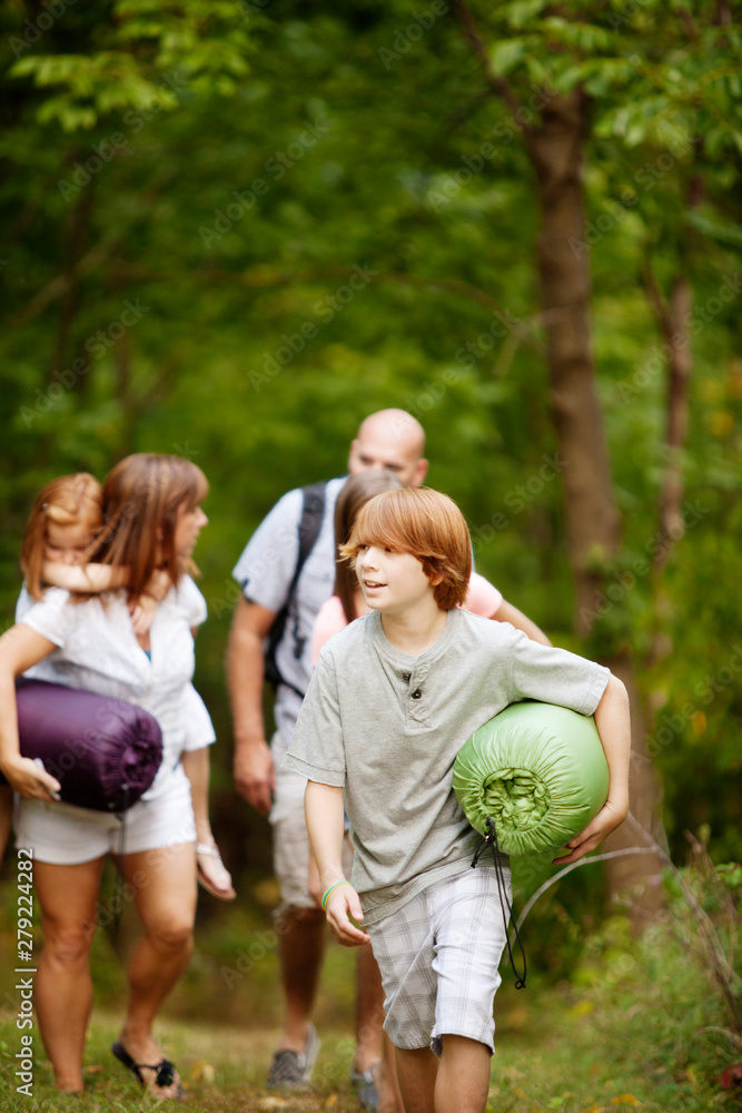 Fototapeta premium Family with three children (6-7, 12-13, 16-17) walking through woods with camping gear