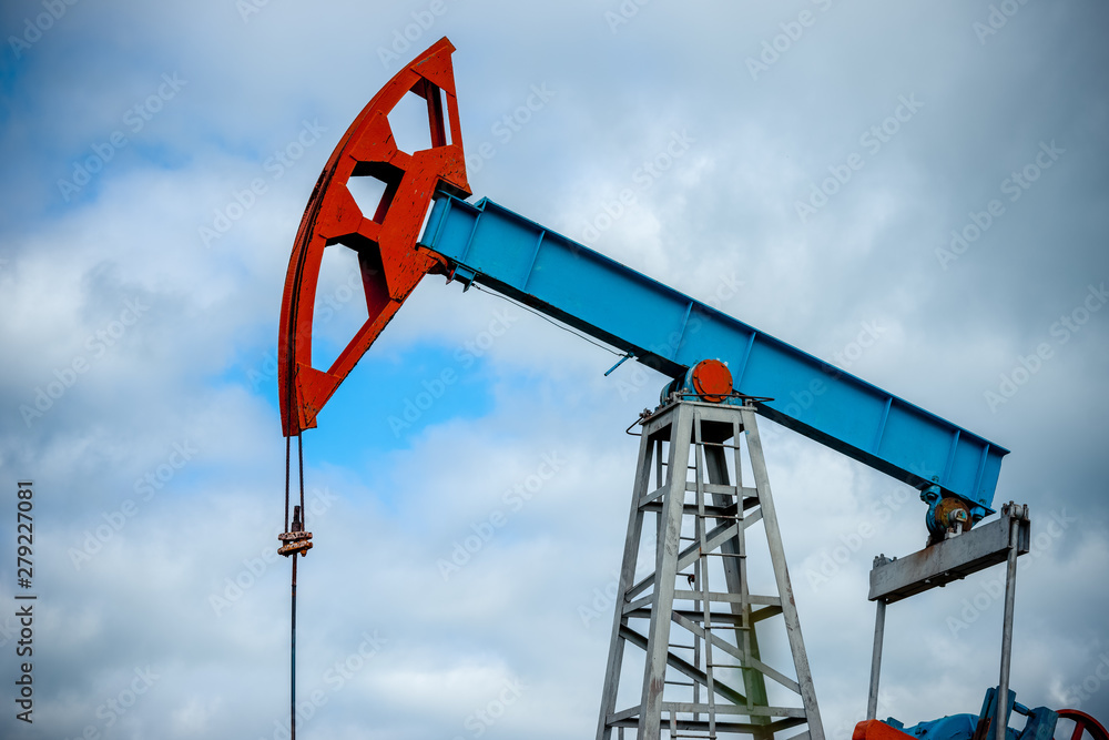 Oil field with pump jack, profiled on blue sky with white clouds, on a sunny day in spring Oil field with pump jack, profiled on blue sky with white clouds, on a sunny day in spring
