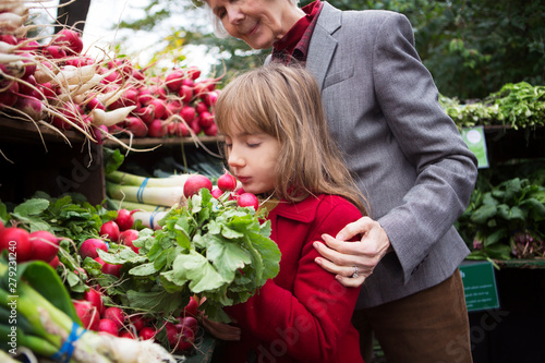 Slika na platnu Grandmother with granddaughter (8-9) choosing vegetables on market
