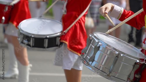 Close-up of female hands drummers are knocking in the drum of their sticks. Street performance of festive march of drummers girls in red costumes on city street. Slow motion