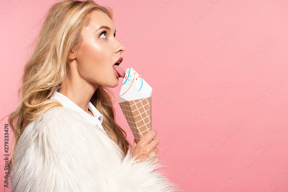 side view of beautiful sexy blonde woman in white faux fur jacket licking decorative ice cream isolated on pink side view of beautiful sexy blonde woman in white faux fur jacket licking decorative ice cream isolated on pink